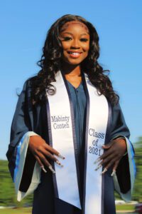 A smiling woman in a graduation gown and sash.