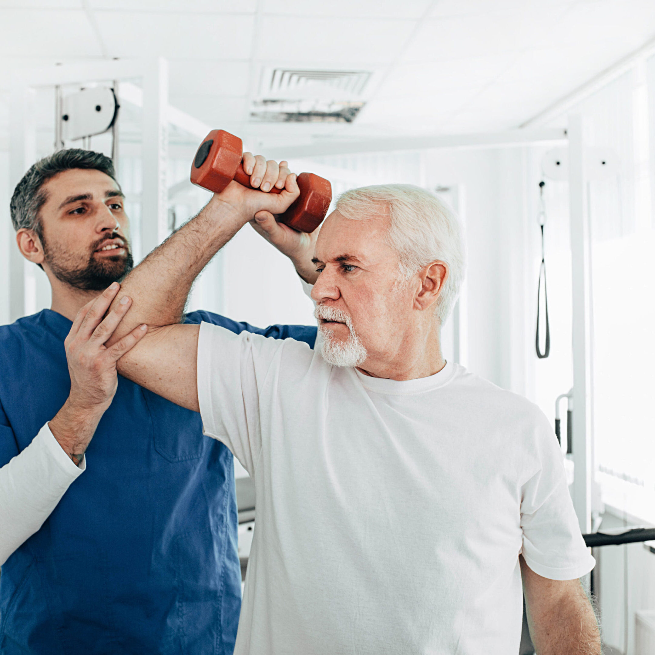 Therapist assisting elderly man with dumbbell exercise.